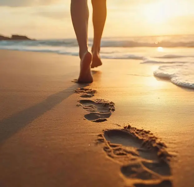 Woman walking along the beach at sunset.